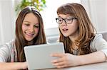 Sisters using digital tablet at table in house