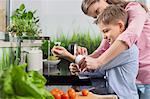 Mother assisting son in folding sleeves while washing hands in kitchen