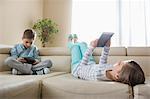 Siblings using technologies on sofa at home