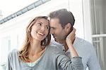 Couple whispering and smiling by window