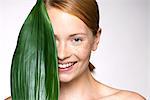 Young woman holding up leaf concealing part of face