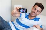 Young man reclining on bed taking selfie with smartphone