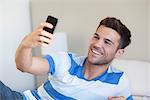 Young man reclining on bed taking selfie with smartphone
