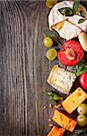 Assortment of delicious cheeses and fruit on a wooden background with copy space for text.