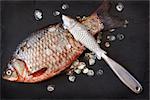 Fresh carp with fish scaler for removal of fish scales on a black slate board.