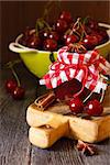 Delicious cherry jam with spices and fresh cherries on a kitchen table.