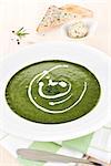 Spinach soup in white plate on wooden table, toast bread and herbal butter in bowl in background.