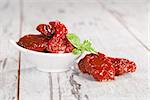Delicious dried tomatoes in white bowl on wooden textured background. Traditional mediterranean kitchen.