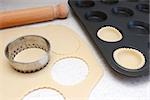 Lining a bun tin with circles of rolled out pastry to make mince pies, with a rolling pin on the worktop