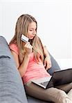 Young woman on sofa thinking what to buy online