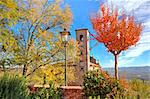 Old brick bell tower as seen among trees with red and yellow leaves in small italian town in autumn.