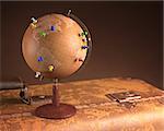 Old globe with pins marking the route of the trip on top a vintage suitcase.