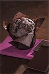 Delicious chocolate muffin with chocolate bar on purple napkin on wooden background. Dark brown culinary sweets.