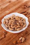 Almonds in white vintage bowl on wooden background. Healthy nuts eating.