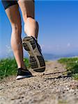 Photo of the legs and shoes of a young woman jogging on a gravel path down a country path.