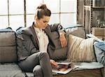 Relaxed business woman sitting on sofa in loft apartment and looking magazine