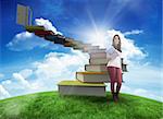 Smiling student holding textbook against green hill under blue sky