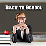 Redhead teacher sitting at desk against red apple on pile of books in classroom