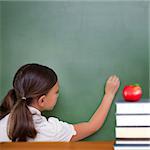 Red apple on pile of books against cute pupil writing on chalkboard