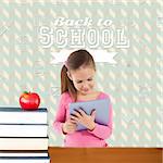 Cute girl using tablet against red apple on pile of books