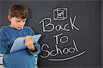 Cute boy using tablet against back to school message on chalkboard