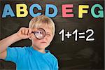 Cute boy looking through a magnifying glass against alphabet magnets stuck on blackboard up to letter g