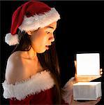 Pretty brunette in santa outfit opening a gift on black background