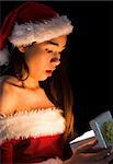 Amazed brunette in santa outfit opening a gift on black background