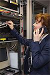 Pretty computer technician talking on phone while fixing server in large data center