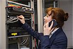 Pretty technician talking on phone while fixing server in large data center