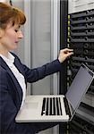 Pretty technician using laptop while working on servers in large data center