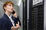 Pretty technician talking on phone while looking at server in large data center