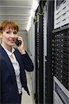 Smiling technician talking on phone while looking at server in large data center