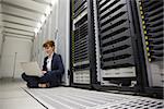 Technician sitting on floor beside server tower using laptop in large data center