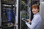 Smiling technician using tablet pc while analysing server in large data center