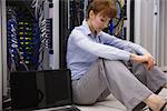 Stressed technician sitting on floor beside open server in large data center