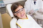 Little girl sitting in dentists chair wearing protective glasses at the dental clinic