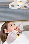 Dentist using mouth retractor on little girl at the dental clinic