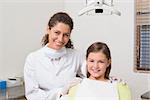 Little girl smiling at camera with her pediatric dentist at the dental clinic