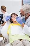 Pediatric dentist examining a little boys teeth with assistant behind at the dental clinic