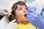 Pediatric dentist examining a little boys teeth with his assistant at the dental clinic
