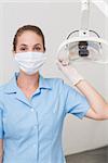 Dental assistant in mask holding light at the dental clinic