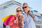 Happy senior couple looking at smartphone holding shopping bags on a sunny day