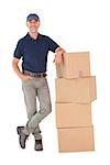 Happy delivery man leaning on pile of cardboard boxes on white background