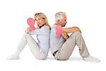 Unhappy couple sitting holding two halves of broken heart on white background