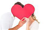 Attractive young couple kissing behind large heart on white background