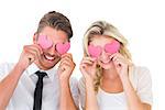 Attractive young couple holding pink hearts over eyes on white background