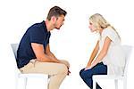 Young couple sitting in chairs arguing on white background