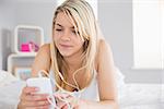 Relaxed young woman listening music with mobile phone in bed at home