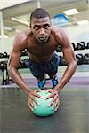 Determined shirtless muscular man doing push ups with ball in the gym